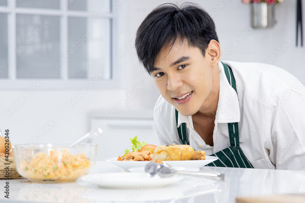 Cute, young and handsome Asian man wearing apron show and pride for his plate of food in modern kitchen