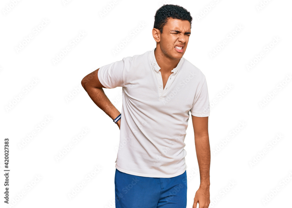 Young arab man wearing casual clothes suffering of backache, touching back with hand, muscular pain Young arab man wearing casual clothes suffering of backache, touching back with hand, muscular pain