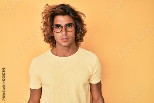 Young hispanic man wearing casual clothes and glasses with serious expression on face. simple and natural looking at the camera.