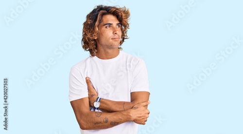 Young hispanic man wearing casual white tshirt looking to the side with arms crossed convinced and confident