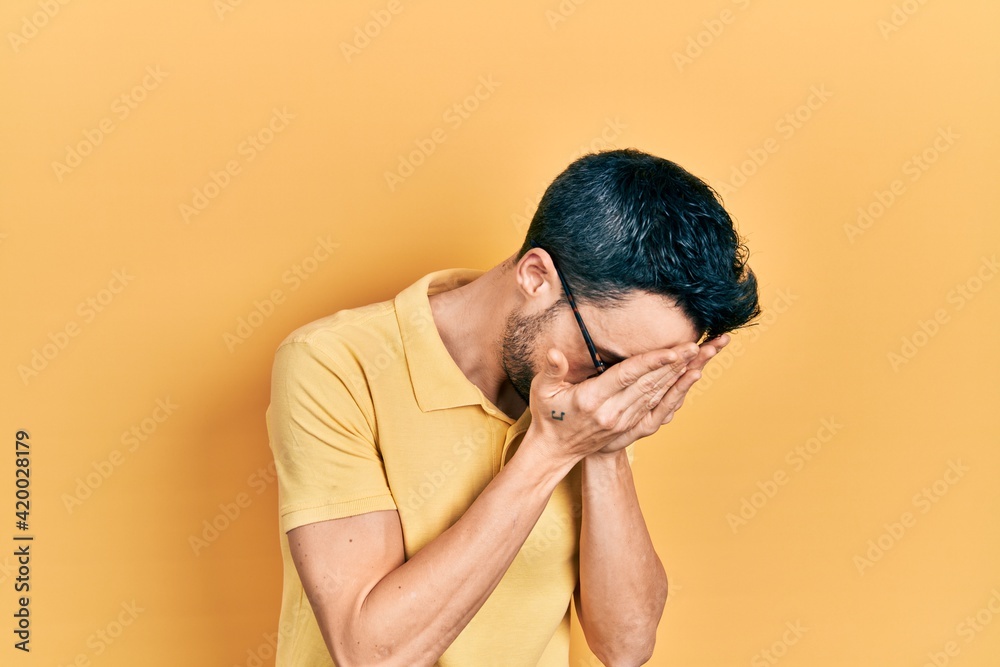 Young hispanic man wearing casual clothes and glasses with sad expression covering face with hands while crying. depression concept. Young hispanic man wearing casual clothes and glasses with sad expression covering face with hands while crying. depression concept.
