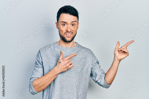 Fotografie Young hispanic man pointing with fingers to the side clueless and confused expression