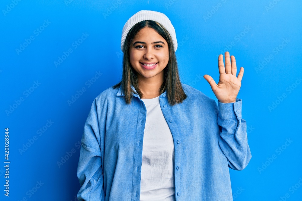 Young latin woman wearing cute wool cap showing and pointing up with fingers number five while smiling confident and happy. Young latin woman wearing cute wool cap showing and pointing up with fingers number five while smiling confident and happy.