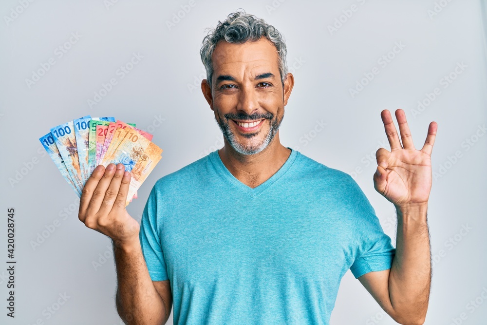 Middle age grey-haired man holding swiss franc banknotes doing ok sign with fingers, smiling friendly gesturing excellent symbol Middle age grey-haired man holding swiss franc banknotes doing ok sign with fingers, smiling friendly gesturing excellent symbol
