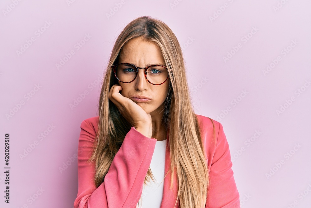 Young blonde woman wearing business style and glasses thinking looking tired and bored with depression problems with crossed arms. Young blonde woman wearing business style and glasses thinking looking tired and bored with depression problems with crossed arms.