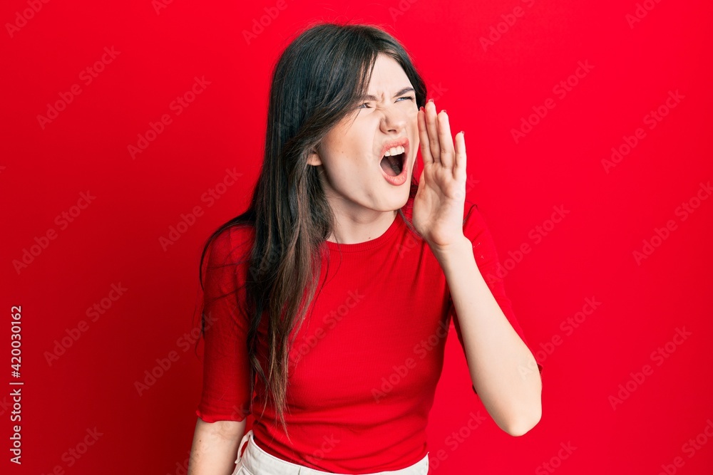 Young beautiful caucasian girl wearing casual red shirt shouting and screaming loud to side with hand on mouth. communication concept. Young beautiful caucasian girl wearing casual red shirt shouting and screaming loud to side with hand on mouth. communication concept.