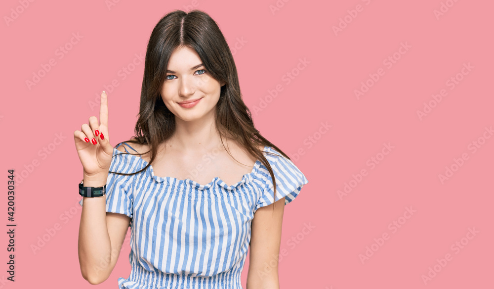 Young beautiful caucasian girl wearing casual clothes showing and pointing up with finger number one while smiling confident and happy. Young beautiful caucasian girl wearing casual clothes showing and pointing up with finger number one while smiling confident and happy.