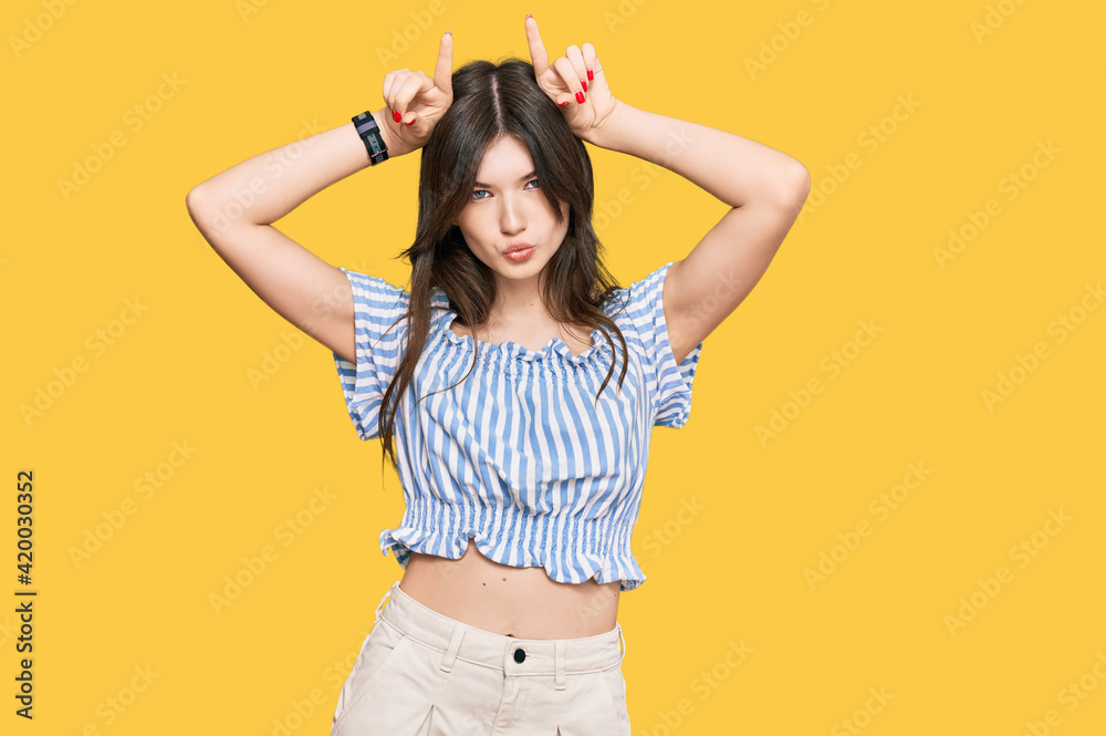 Young beautiful caucasian girl wearing casual clothes doing funny gesture with finger over head as bull horns