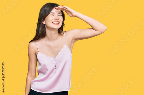 Young beautiful caucasian girl wearing casual clothes very happy and smiling looking far away with hand over head. searching concept.