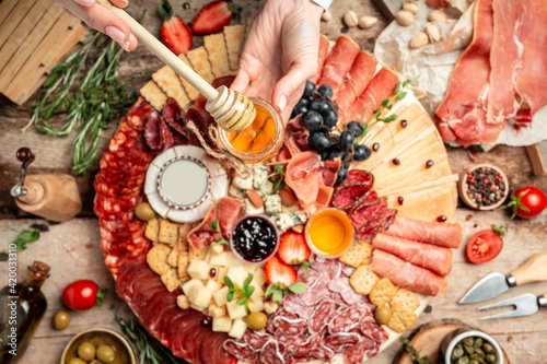 Antipasto with traditional Spanish meat snacks on wooden board. Women's hands holding honey, Antipasto platter. catering, banner, menu, recipe. top view