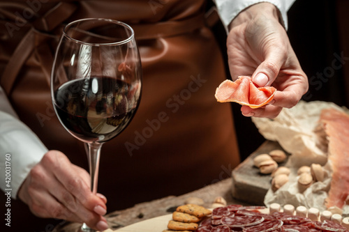 Hands holding a glass of wine and a wooden board with different kinds of cheese and ham, prosciutto, jamon salami, Antipasto Dinner or aperitivo party concept