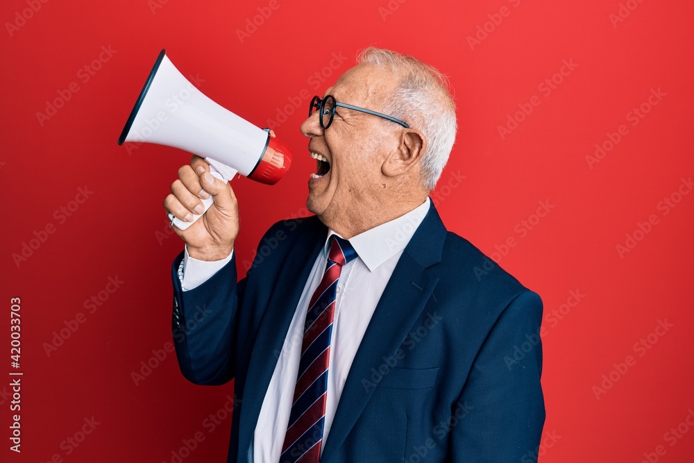 Senior grey-haired businessman screaming using megaphone over isolated red background. Senior grey-haired businessman screaming using megaphone over isolated red background.