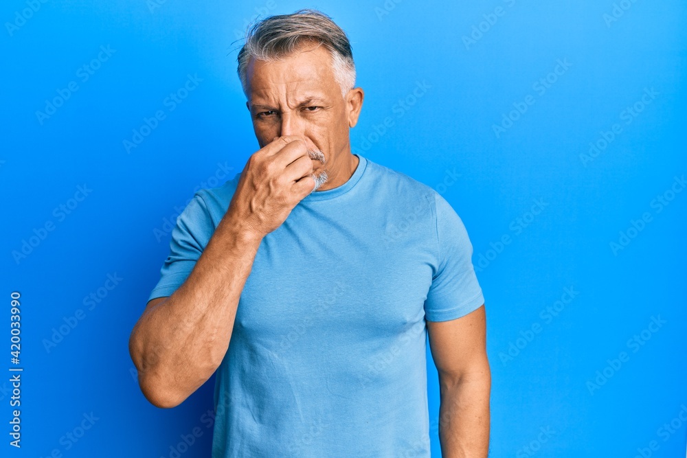 Middle age grey-haired man wearing casual clothes smelling something stinky and disgusting, intolerable smell, holding breath with fingers on nose. bad smell Middle age grey-haired man wearing casual clothes smelling something stinky and disgusting, intolerable smell, holding breath with fingers on nose. bad smell