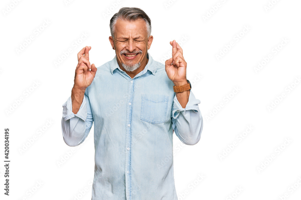 Middle age grey-haired man wearing casual clothes gesturing finger crossed smiling with hope and eyes closed. luck and superstitious concept. Middle age grey-haired man wearing casual clothes gesturing finger crossed smiling with hope and eyes closed. luck and superstitious concept.