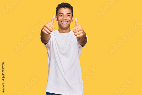 Young handsome african american man wearing casual white tshirt approving doing positive gesture with hand, thumbs up smiling and happy for success. winner gesture.