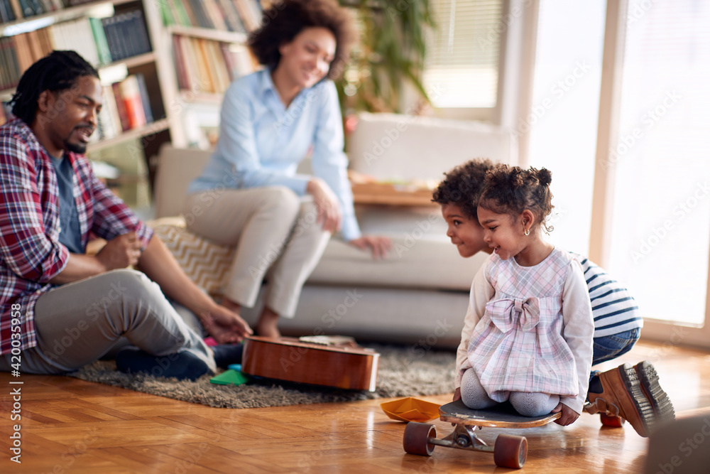 Kids riding skateboard on the floor and enjoying the playtime with their parents at home. Family, together, love, playtime Kids riding skateboard on the floor and enjoying the playtime with their parents at home. Family, together, love, playtime