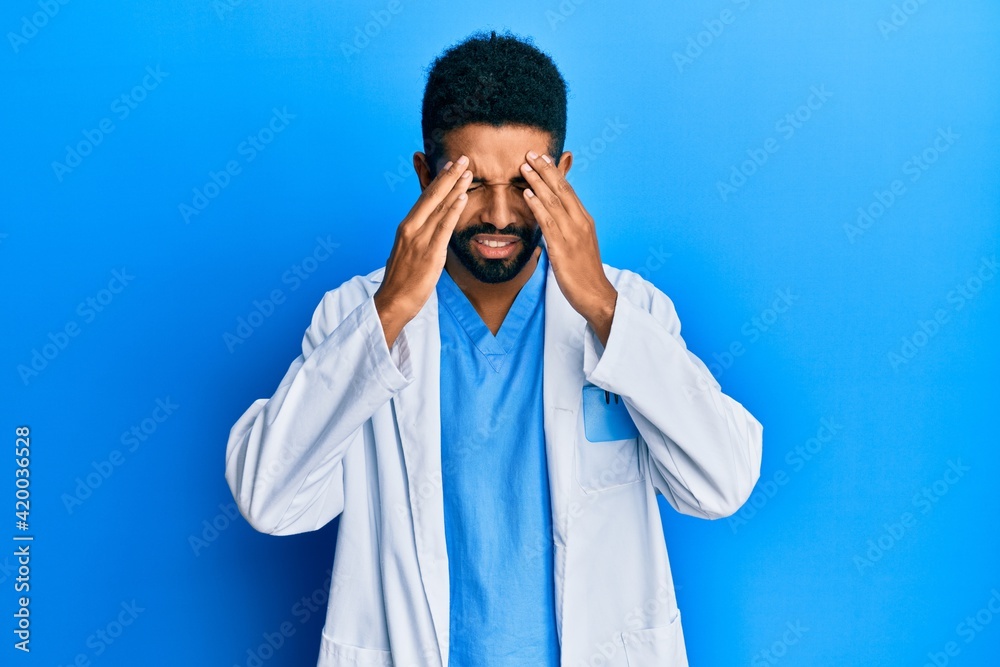 Handsome hispanic man with beard wearing doctor uniform with hand on head for pain in head because stress. suffering migraine. Handsome hispanic man with beard wearing doctor uniform with hand on head for pain in head because stress. suffering migraine.