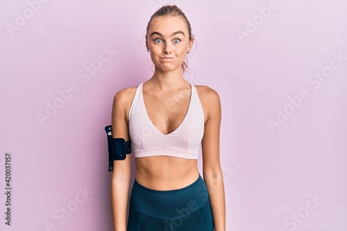 Beautiful blonde woman wearing sportswear and arm band puffing cheeks with funny face. mouth inflated with air, crazy expression. © Krakenimages.com