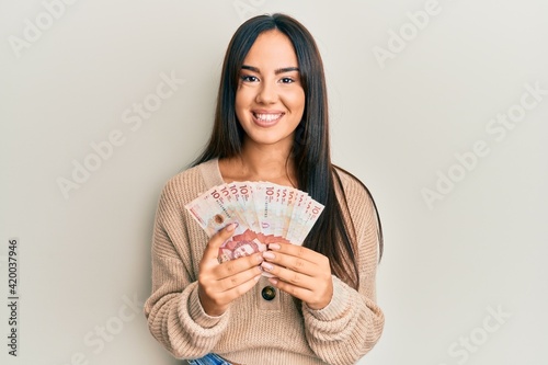 Young beautiful hispanic girl holding 10 colombian pesos banknotes smiling with a happy and cool smile on face. showing teeth.