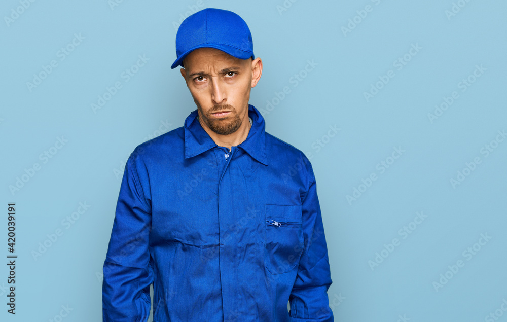 Bald man with beard wearing builder jumpsuit uniform skeptic and nervous, frowning upset because of problem. negative person. Bald man with beard wearing builder jumpsuit uniform skeptic and nervous, frowning upset because of problem. negative person.