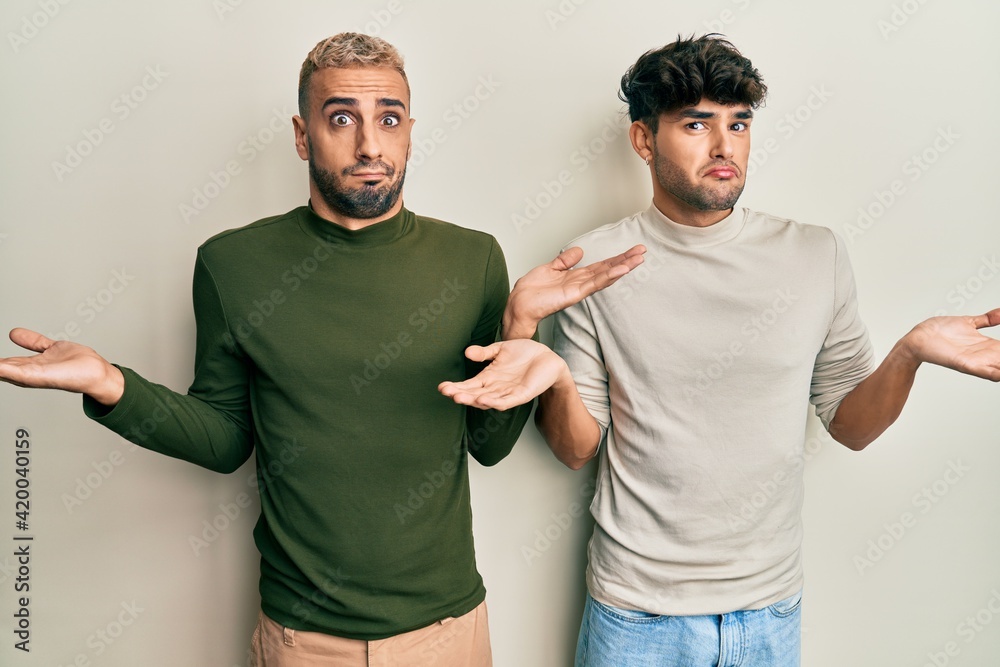 Fotka „Homosexual gay couple standing together wearing casual clothes  clueless and confused with open arms, no idea and doubtful face.“ ze služby  Stock | Adobe Stock