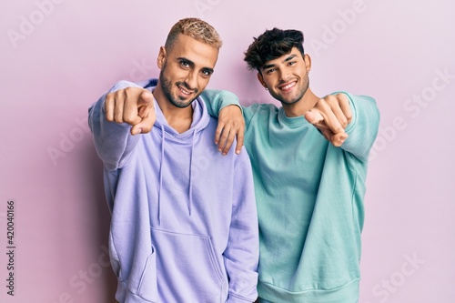 Homosexual gay couple standing together wearing casual clothes pointing to you and the camera with fingers  smiling positive and cheerful