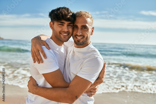 Young gay couple smiling happy hugging at the beach.