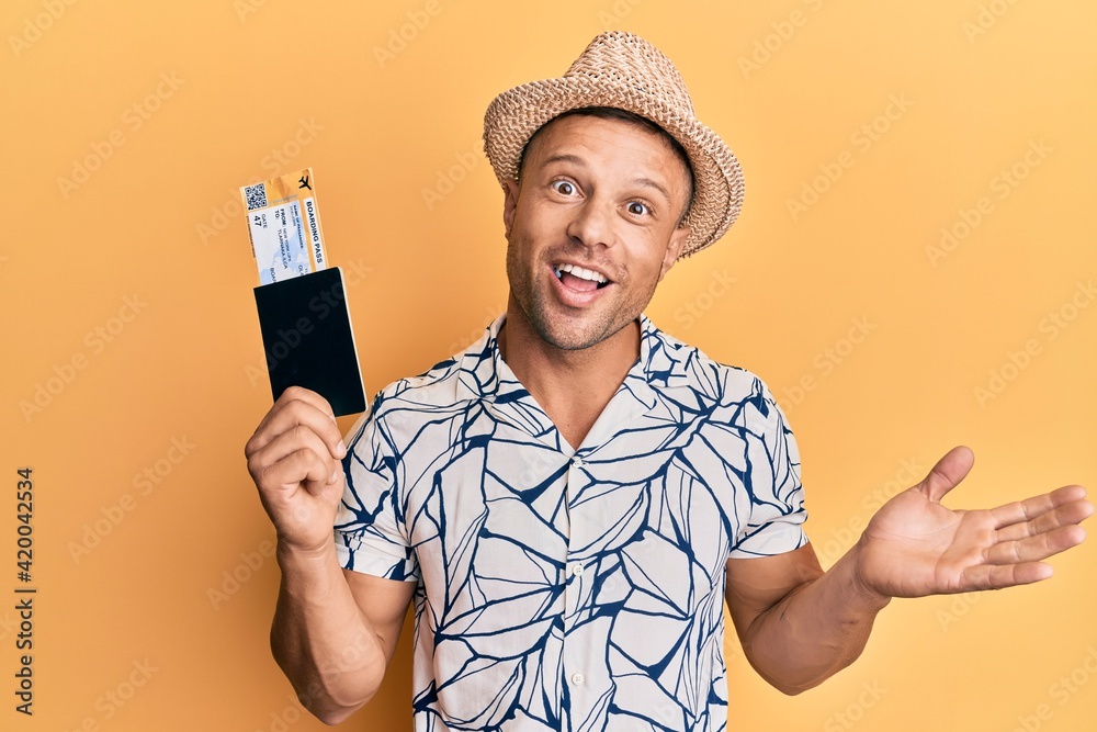 Handsome muscle man holding boarding pass and passport celebrating achievement with happy smile and winner expression with raised hand Handsome muscle man holding boarding pass and passport celebrating achievement with happy smile and winner expression with raised hand