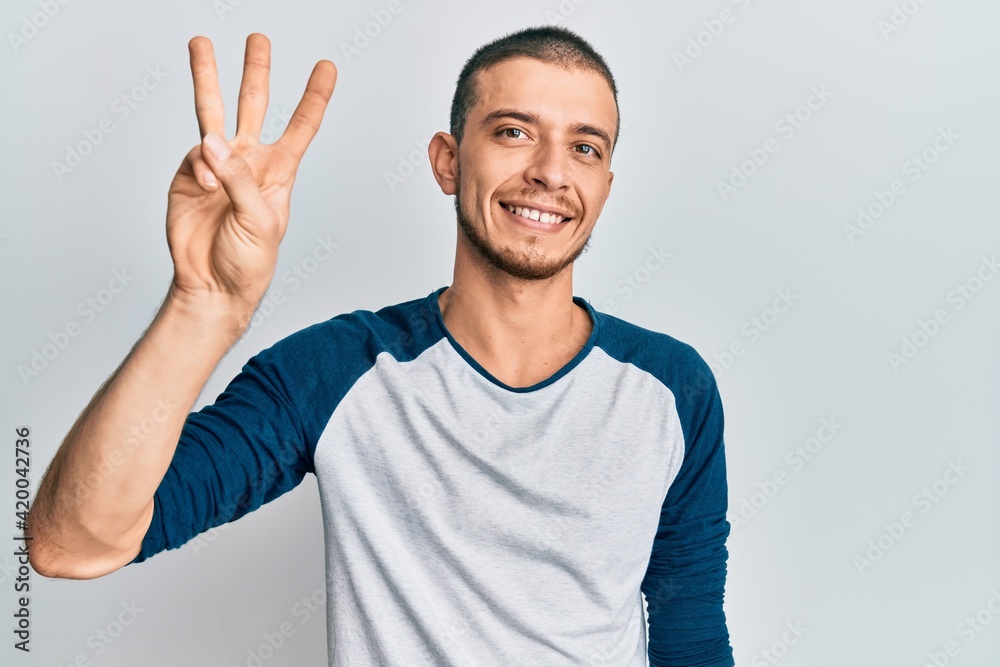 Hispanic young man wearing casual clothes showing and pointing up with fingers number three while smiling confident and happy. Hispanic young man wearing casual clothes showing and pointing up with fingers number three while smiling confident and happy.