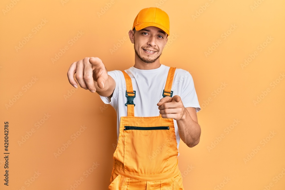 Hispanic young man wearing handyman uniform pointing to you and the camera with fingers, smiling positive and cheerful Hispanic young man wearing handyman uniform pointing to you and the camera with fingers, smiling positive and cheerful