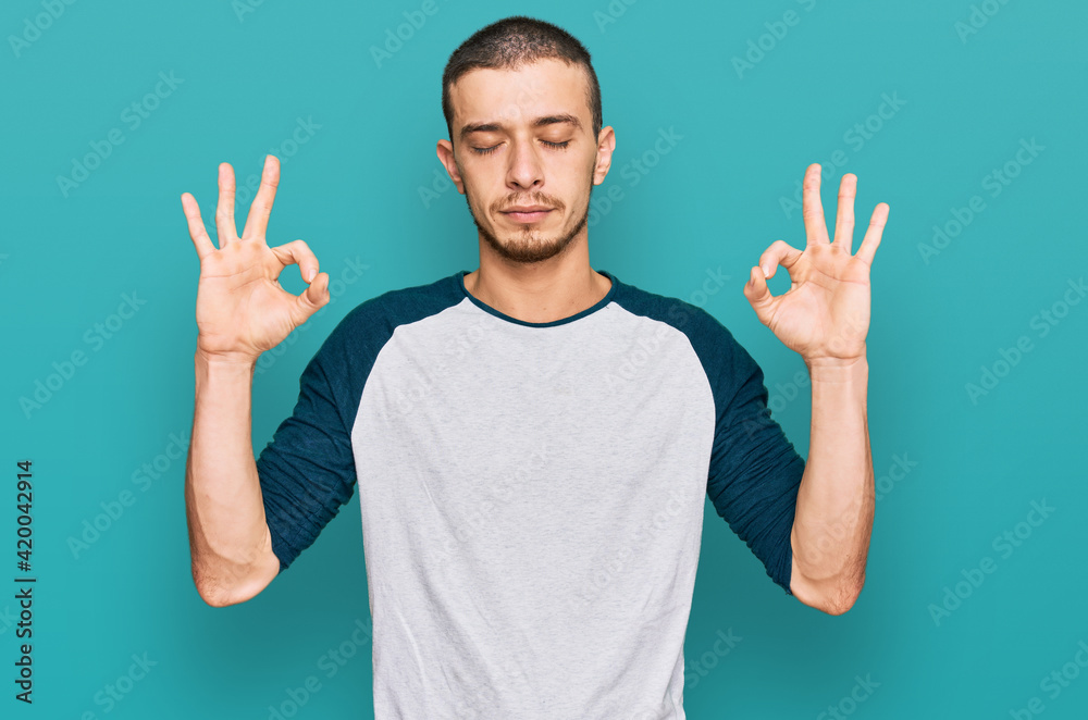Hispanic young man wearing casual clothes relax and smiling with eyes closed doing meditation gesture with fingers. yoga concept. Hispanic young man wearing casual clothes relax and smiling with eyes closed doing meditation gesture with fingers. yoga concept.