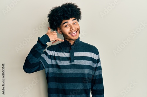 Young african american man with afro hair wearing casual clothes smiling doing phone gesture with hand and fingers like talking on the telephone. communicating concepts.