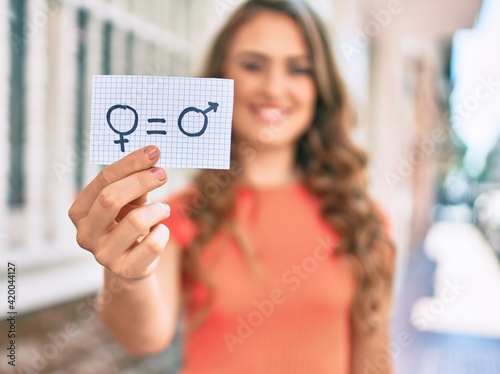 Young blonde girl smiling happy holding paper with gender equality concept walking at the city.