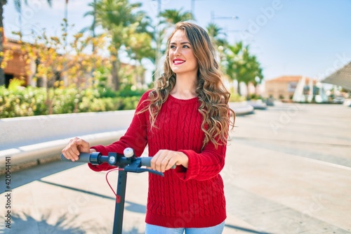 Young blonde girl smiling happy using electric scooter at the park.