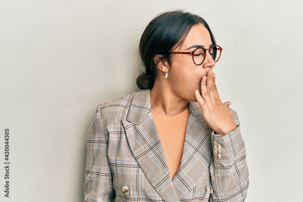 Young brunette woman wearing business jacket and glasses bored yawning tired covering mouth with hand. restless and sleepiness.
