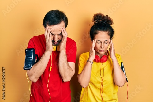 Middle age couple of hispanic woman and man wearing sportswear and arm band with hand on head for pain in head because stress. suffering migraine.