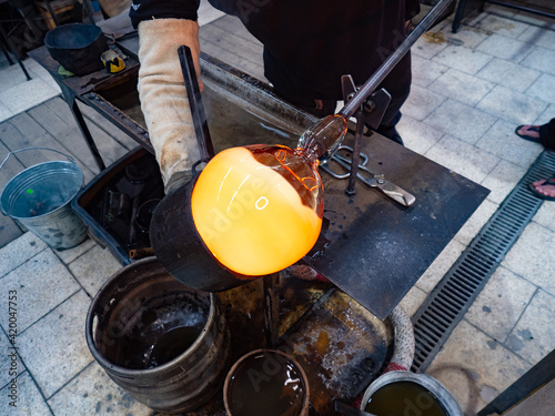 Artisan hands forming the red malleable glass on glassblower whistle.