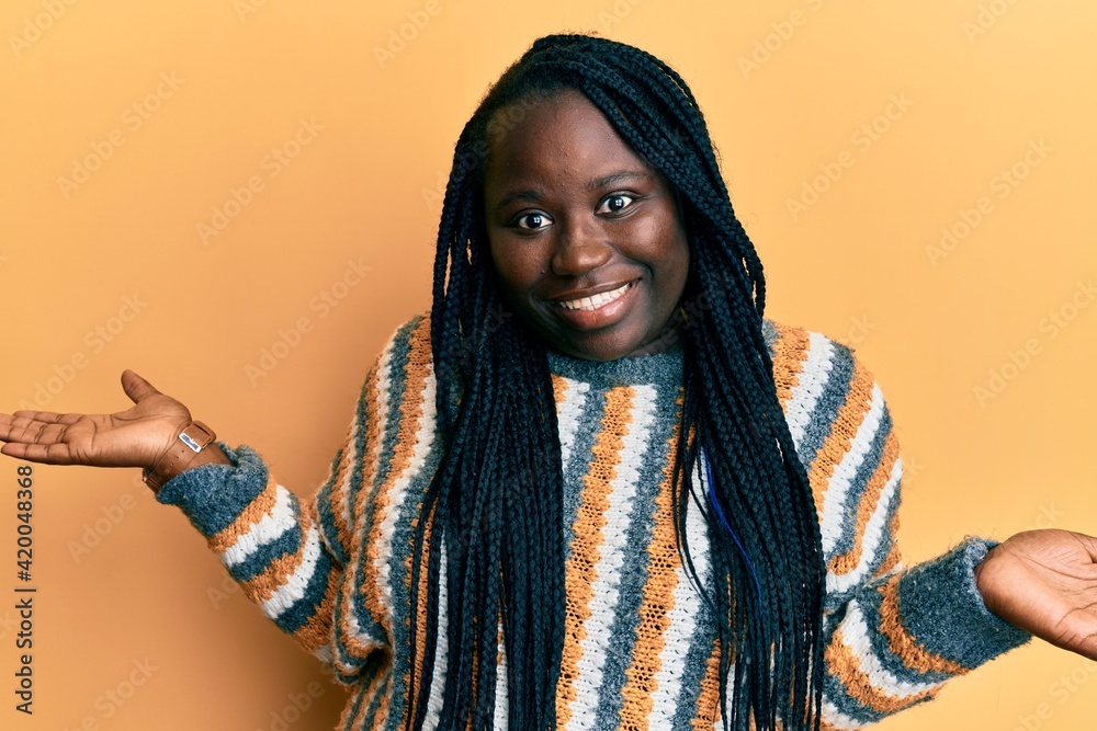 Young black woman with braids wearing casual winter sweater smiling showing both hands open palms, presenting and advertising comparison and balance Young black woman with braids wearing casual winter sweater smiling showing both hands open palms, presenting and advertising comparison and balance