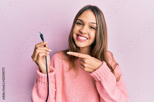 Young brunette woman holding ethernet rj45 cable smiling happy pointing with hand and finger