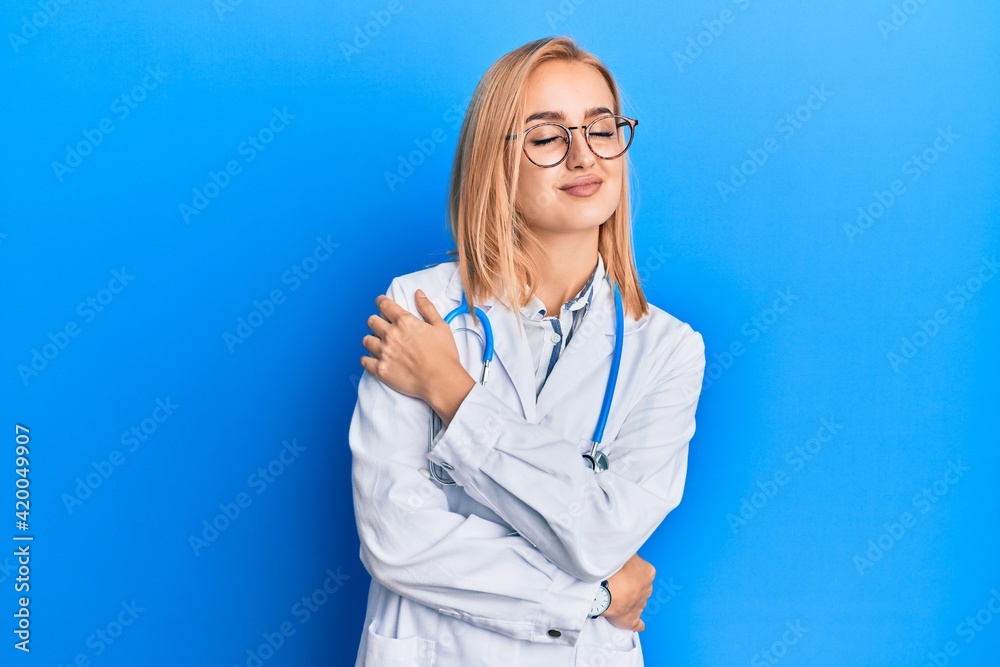 Beautiful caucasian woman wearing doctor uniform hugging oneself happy and positive, smiling confident. self love and self care