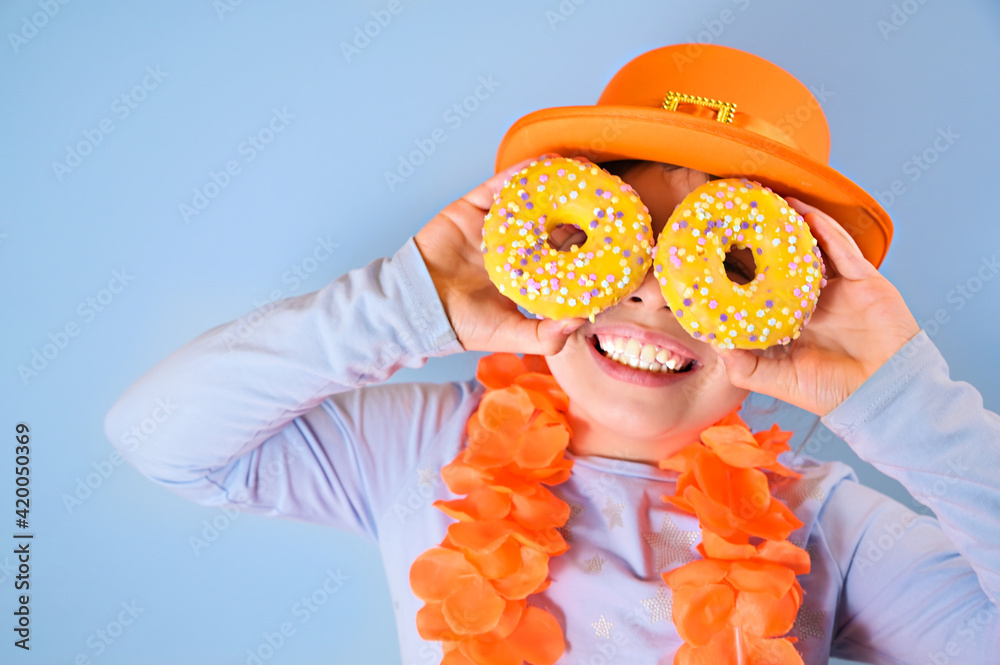 Fotka „King's Day in Holland. Traditional festival on April 27 in the  Netherlands. A little girl in a festive orange hat holds in hands colored  donuts. Copy space“ ze služby Stock