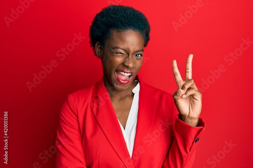 Young african american girl wearing business clothes smiling with happy face winking at the camera doing victory sign. number two.