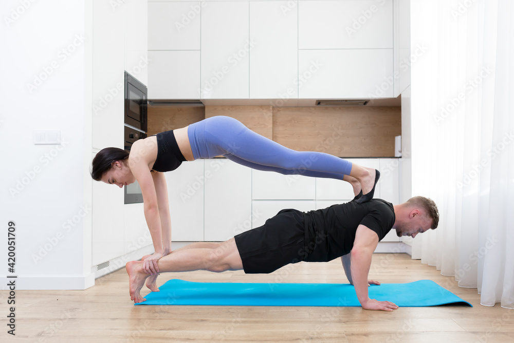young couple man and woman doing fitness together at home on the floor, two people doing sports exercises in the kitchen on a sports mat young couple man and woman doing fitness together at home on the floor, two people doing sports exercises in the kitchen on a sports mat