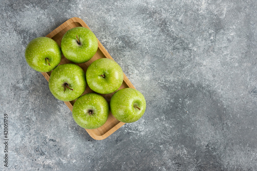 Wooden plate of shiny green apples on marble background