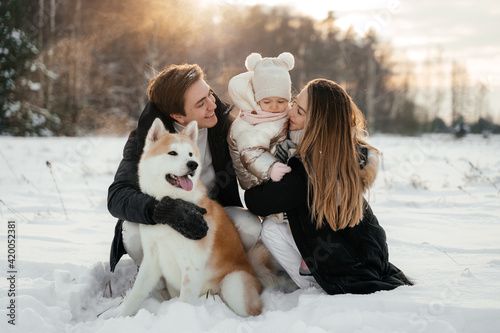 Young parernts holding small daughter in winter forest with akita dog