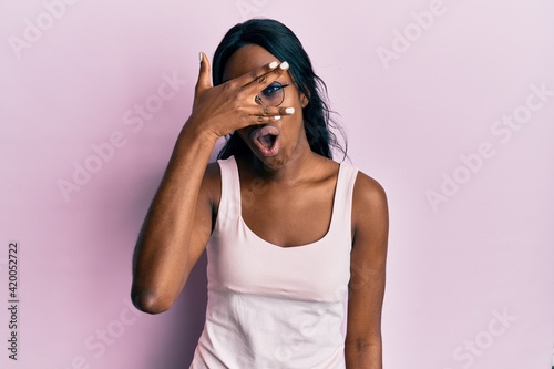 Young african american woman wearing casual clothes and glasses peeking in shock covering face and eyes with hand, looking through fingers afraid