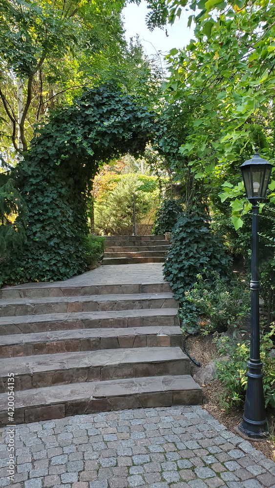 Path through arched gateway to English walled garden. Stone paved stairs in park with retro streetlight lantern Path through arched gateway to English walled garden. Stone paved stairs in park with retro streetlight lantern