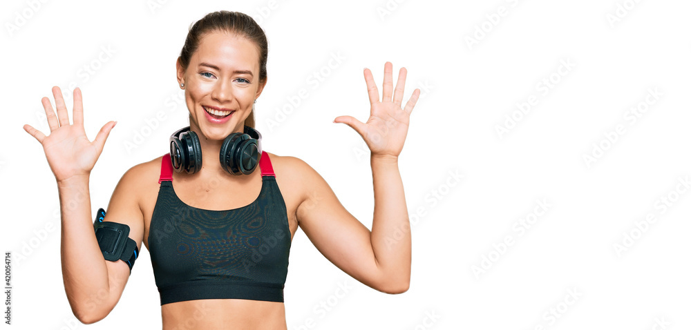 Beautiful blonde woman wearing gym clothes and using headphones showing and pointing up with fingers number ten while smiling confident and happy. Beautiful blonde woman wearing gym clothes and using headphones showing and pointing up with fingers number ten while smiling confident and happy.