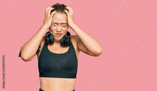 Beautiful blonde woman wearing gym clothes and using headphones suffering from headache desperate and stressed because pain and migraine. hands on head.