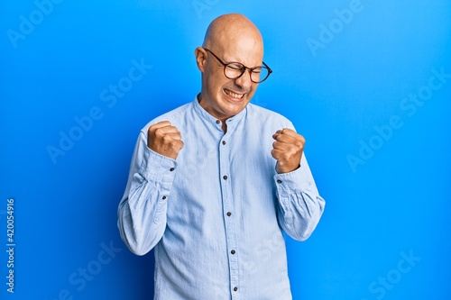 Middle age bald man wearing casual clothes and glasses excited for success with arms raised and eyes closed celebrating victory smiling. winner concept.